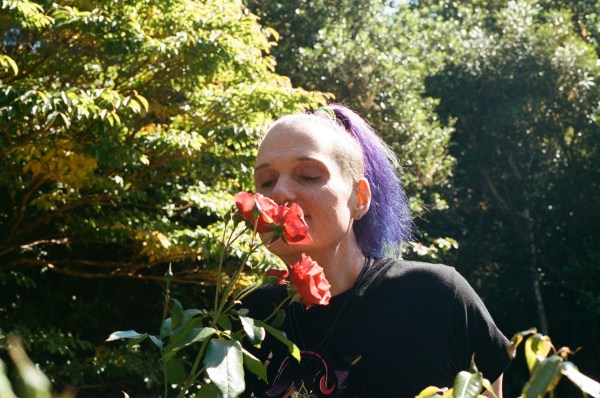 Person with purple hair smelling a bouquet of pink flowers