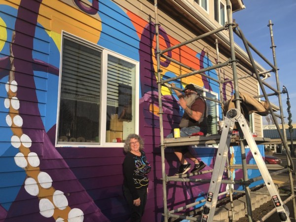 Donna Bader, the new owner of Bader Fine Art Gallery, talks with muralist Gary Herd about the large, bright octopus he’s painting on the side of her building in downtown Waldport. Photo by: Quinton Smith/YachatsNews.com