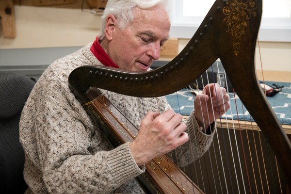 David Rivinus plays the newly restored, 100-year-old harp in the workshop of his Yachats home. “My job was to redo their work, but do it right,” he says. Photo by: Jordan Essoe