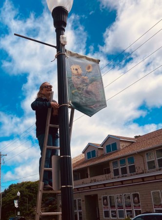 Veronica Lundell, founder of the Nye Beach Banner Project, hangs a banner last spring in the Newport neighborhood. Lundell suffered a serious head injury Oct. 21 when her ladder gave way while she was removing a banner for the November auction. Photo by: Erin Tormey