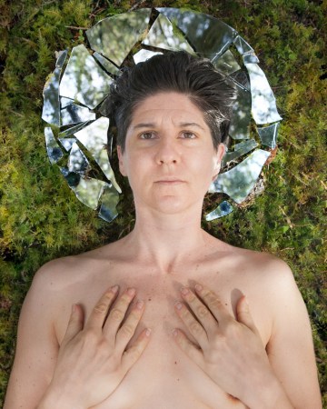 Human bust with hands over chest area, eyes look straight out at viewer with head against a broken mirror circle